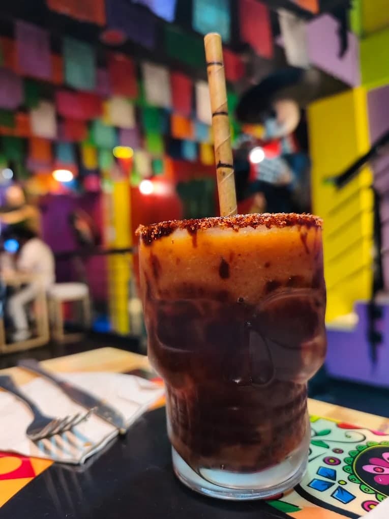 Coctel servido en un vaso con forma de calavera, escarchado con tajín